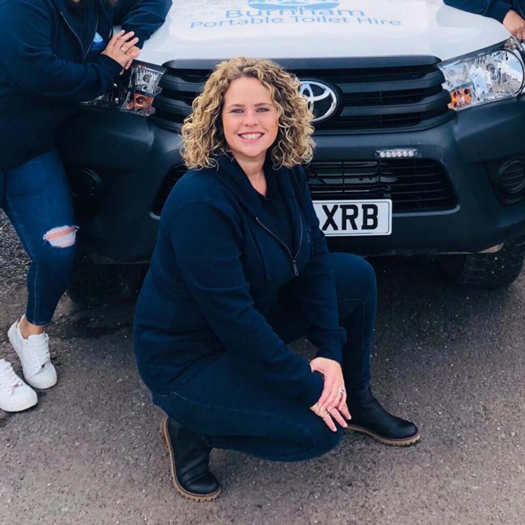 Becky of Burnham Portable Toilet Hire family company, photo of her smiling in front of a branded logo fleet vehicle